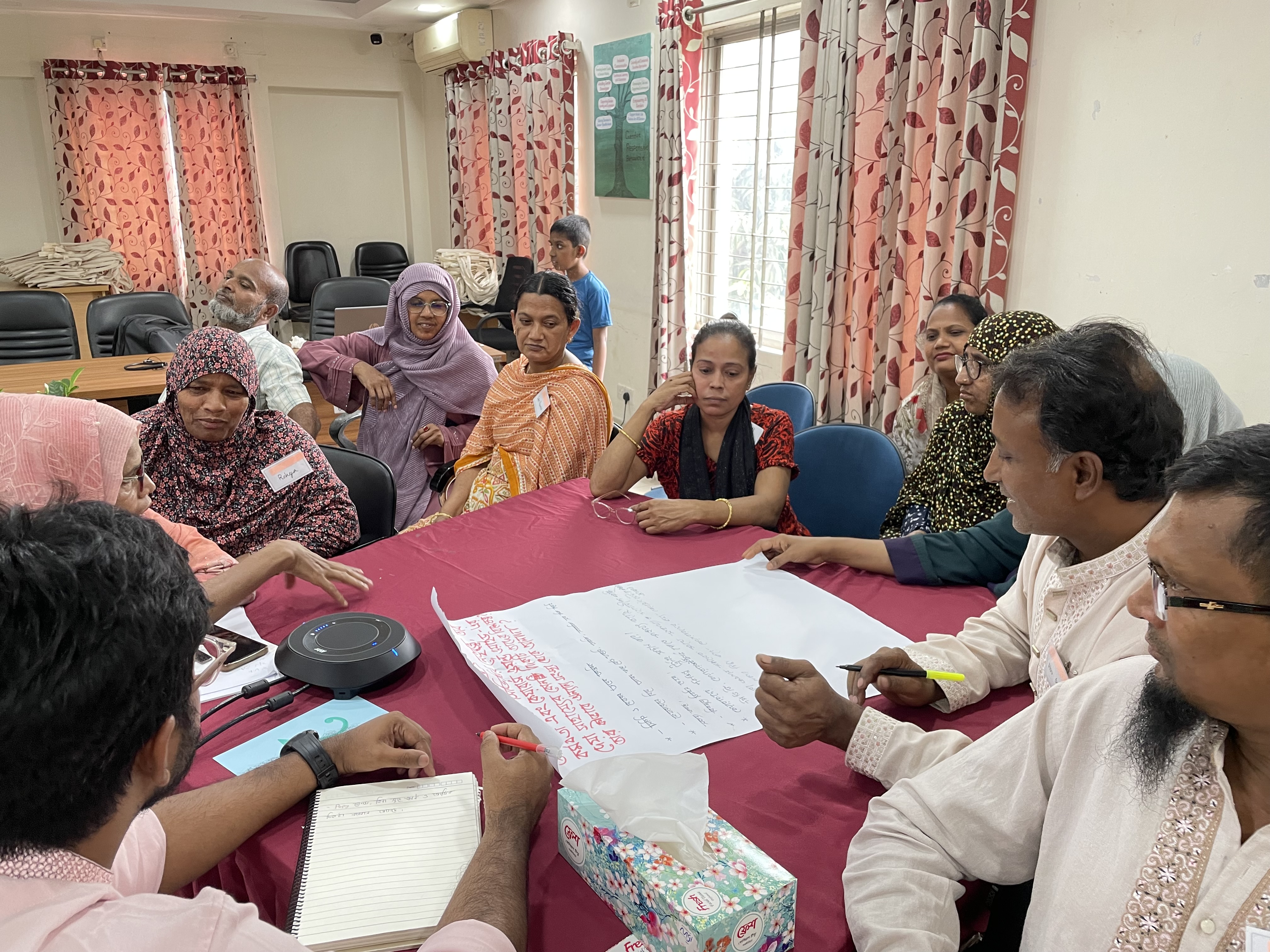 Participants gather around a table to discuss findings from Bangladesh.