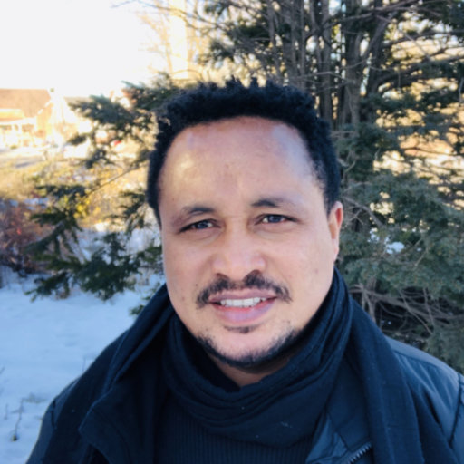 A headshot of Dr. Molalign Adunga who smiles at the camera. He is standing in front of a snowy background.