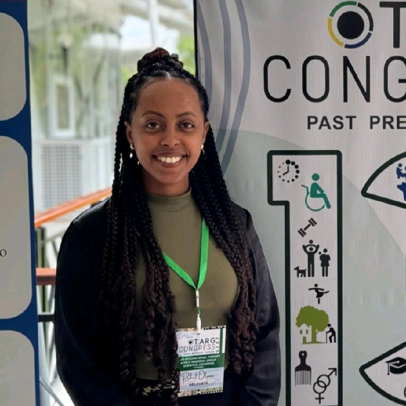 Rahel Olana stands, wearing a black blazer on top of a green tee. She is smiling at the camera.