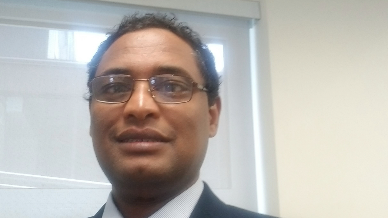 Dr. Bekele Worku smiles at the camera. He is wearing a blazer and shirt, with glasses.