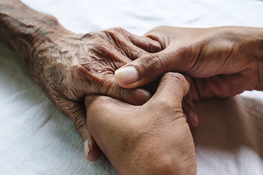 The hand of an elderly person is held with two hands of a younger person.