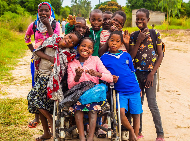 group of children smiling surrounding smiling girl in wheelchair on dirt road in Mozambique
