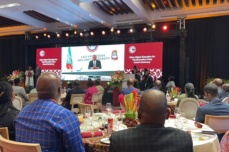 A view of the event space from Heather's perspective, sat at a roundtable, looking at the stage which has a large screen as its backdrop, displaying the name of the event.