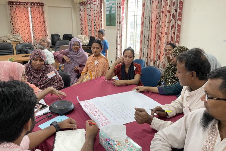 Participants gather around a table to discuss findings from Bangladesh.