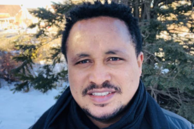 A headshot of Dr. Molalign Adunga who smiles at the camera. He is standing in front of a snowy background.