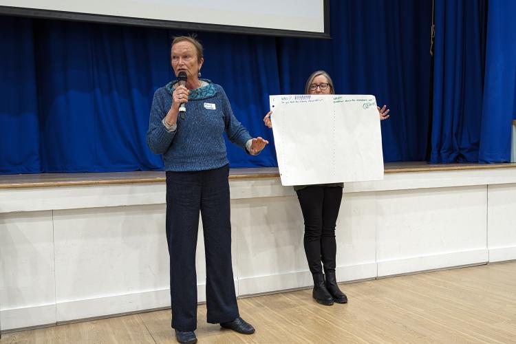 Mary Wickenden (L) points to a blank sheet of paper that details the activity that participants will complete. The paper is held by Ruth Patil.