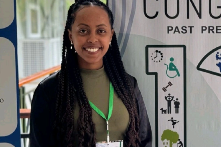 Rahel Olana stands, wearing a black blazer on top of a green tee. She is smiling at the camera.