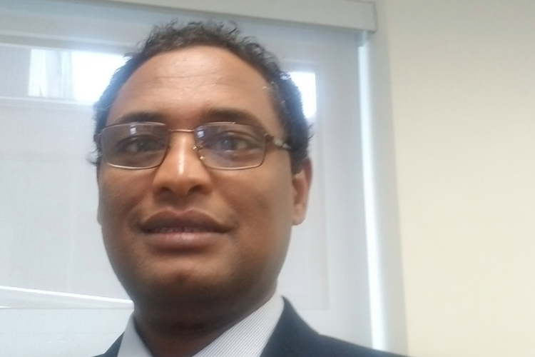 Dr. Bekele Worku smiles at the camera. He is wearing a blazer and shirt, with glasses.