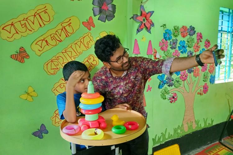 PhD student Krishno stands with a young child. They are playing with some toys on a table.