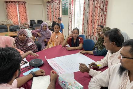Participants gather around a table to discuss findings from Bangladesh.