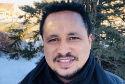 A headshot of Dr. Molalign Adunga who smiles at the camera. He is standing in front of a snowy background.