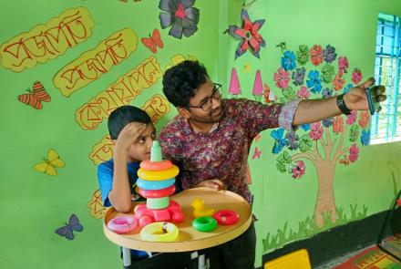 PhD student Krishno stands with a young child. They are playing with some toys on a table.